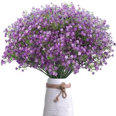 purple flowers are in a white vase with a brown ribbon tied around the top and bottom