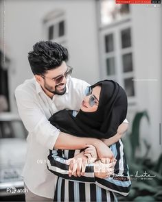 a man holding a woman in his arms while she is wearing sunglasses and a hijab