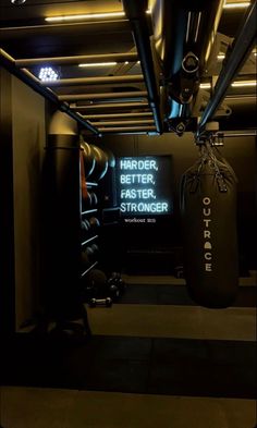 an indoor gym area with punching bags and neon sign on the wall that says harder, faster, stronger