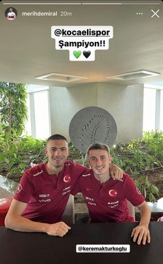 two men in red shirts sitting at a table with their arms around each other's shoulders