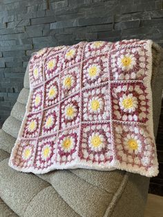 a crocheted pillow sitting on top of a couch next to a brick wall