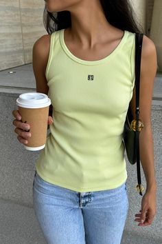 a woman holding a coffee cup in her right hand and wearing a yellow tank top