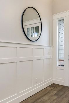 an empty room with white walls and wood flooring is pictured in this image, there is a round mirror on the wall above the door