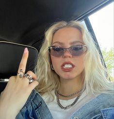 a blonde woman with sunglasses on holding her finger up in the back seat of a car