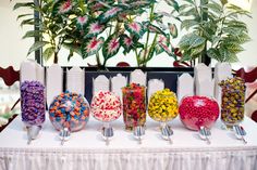 a table topped with lots of different types of candies next to potted plants