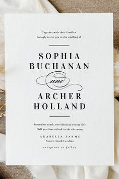 the wedding stationery is laid out on top of an ivory cloth with feathers in it