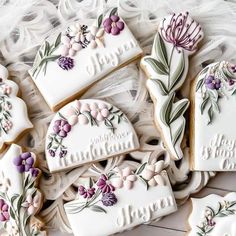 some decorated cookies are laying on a white lace tablecloth with purple flowers and leaves