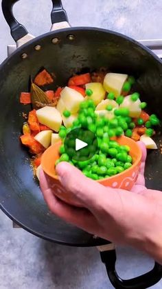 a person holding a bowl filled with peas and carrots on top of a stove