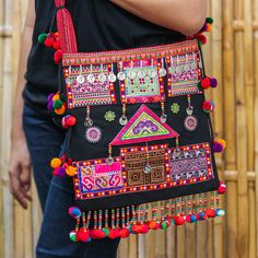 The beauty of the Hmong arts inspires a glorious shoulder bag made in their people's honor. Featuring traditional details made by hand, this colorful accessory with a black base hue is presented by Thai artisan Kunlaya Pangsiri, who adds embroidered details and pompoms to her design. On top of that, the piece has little leaf boxwood, aluminum and plastic beads for a unique touch and comes equipped with two interior pockets and a zipper closure. Hmong Food, Hmong Fashion, Hmong Embroidery, Hmong Clothes, Afghan Clothes, Colorful Accessories, Denim Diy, Boutique Dress Designs, Plastic Beads