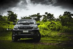 the front end of a black suv parked in a grassy area with trees and bushes