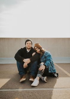 a man and woman sitting on the ground in an empty parking lot with their arms around each other