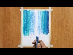 someone is drawing with colored pencils on the paper in front of a wooden wall