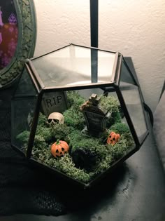 a glass terrarium with fake pumpkins and skulls in the center, sitting on a table