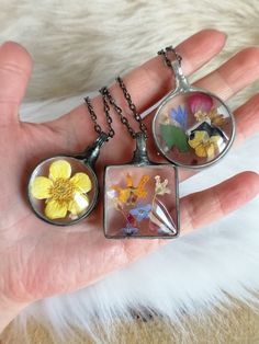 two pieces of glass with flowers in them on a person's hand, one being held by a chain