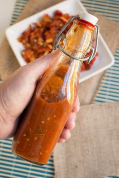 a hand holding a bottle filled with sauce on top of a table next to a plate of food