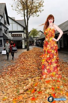 a woman in a dress made out of leaves standing on the ground with her hands on her hips