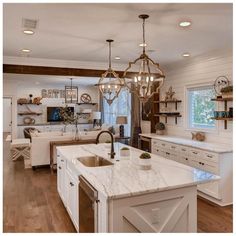 an open concept kitchen and living room with white cabinets, marble counter tops, wood flooring and chandelier hanging from the ceiling