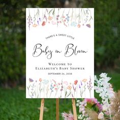 a baby in bloom welcome sign is on an easel with flowers and greenery