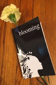 a book with the title blooming next to a flower on a wooden table top