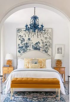 a white bed sitting under a blue chandelier