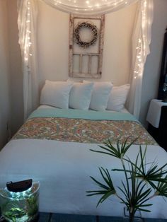 a bed with lights on the headboard and pillows in front of it, next to a potted plant