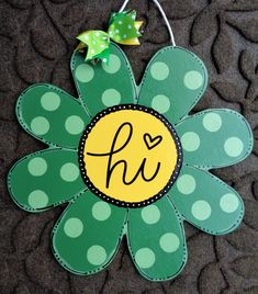 a green and yellow flower with the letter h on it's center is hanging from a hook