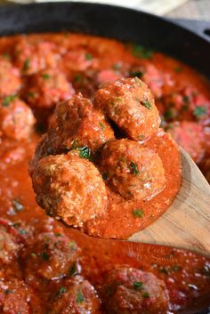 a wooden spoon full of meatballs and sauce