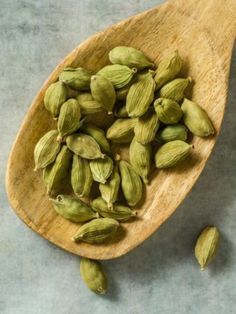 a wooden spoon filled with green cardamoa seeds on top of a gray surface