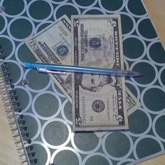 two bills and a pen on top of a notebook with polka dot pattern paper cover