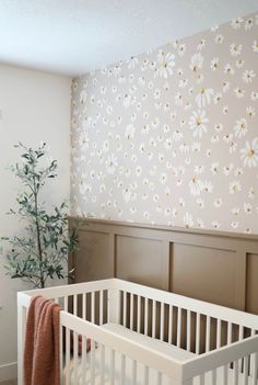 a white crib in front of a wall with flowers on it and a tree