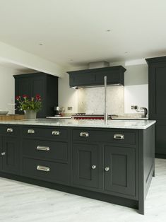 a large kitchen with black cabinets and marble counter tops is pictured in this image, there are flowers on the island