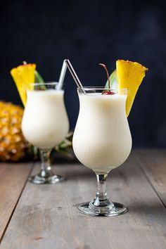 two glasses filled with white liquid and topped with pineapples on a wooden table