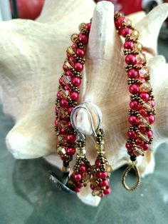 a pair of red and gold beaded bracelets sitting on top of a seashell