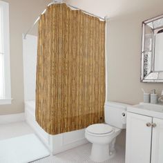 a white toilet sitting next to a bath tub in a bathroom under a window with a bamboo shower curtain