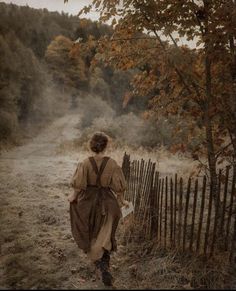 a woman walking down a dirt road next to a wooden fence