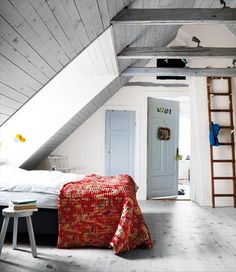 an attic bedroom with white walls and wood flooring is furnished with a red blanket