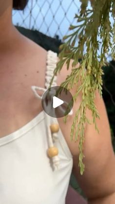 a woman wearing a white top holding a green tree branch in her right hand and looking at the camera