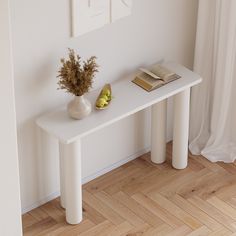 a white table with a book, vase and fruit on it