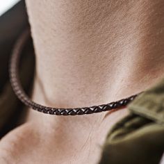 a close up of a person wearing a brown leather necklace with braiding on it