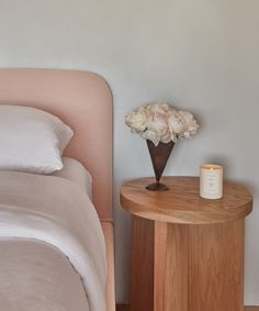 a vase with flowers sitting on a small table next to a bed