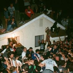 a large group of people are gathered around a house and one person is on the roof