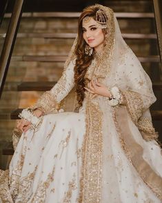 a woman in a white and gold wedding dress sitting on stairs with her hair pulled back