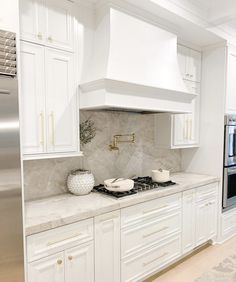 a white kitchen with marble counter tops and gold trim on the oven hood, stove