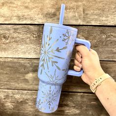 a person is holding a blue cup with gold designs on it while standing against a wooden wall