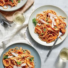 two plates of pasta with sauce and parmesan cheese on the side next to wine glasses