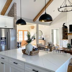 an open kitchen and living room area with white cabinets, black pendant lights over the island