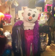 a snowman dressed in purple and pink is standing next to other people at a party