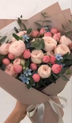 a bouquet of pink roses and blue flowers in a brown paper wrapper with greenery