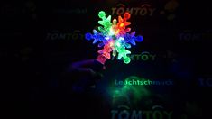 a person is holding up a colorful snowflake in the dark with lights shining on it