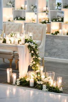 a table with candles, flowers and greenery on it in front of some chairs